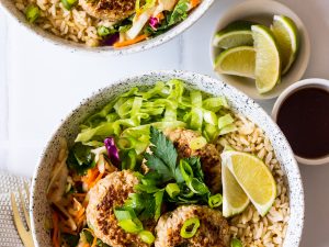 Speckled bowls with brown rice, pork patties, salad, herbs and lime