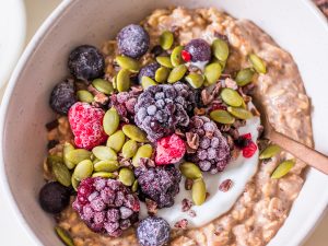 Small white ceramic bowl with chocolate protein overnight oats, yoghurt, berries, cacao nibs and pumpkin seeds