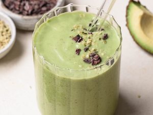 Avocado, banana and spinach green smoothie in a clear glass with a glass straw