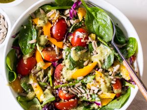 Image of a tuna salad with baby spinach, capsicum, cabbage and cherry tomatoes in a speckled white bowl