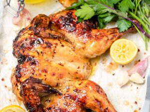 Flattened roast chicken with lemon pieces, fresh parsley and jar of pan juices