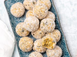 Blue rectangular plate with apricot bliss balls on top rolled in coconut, white table background