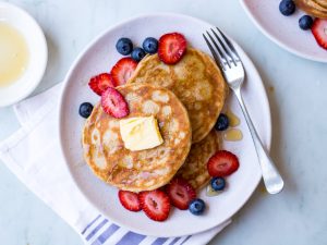 gluten free buckwheat pancakes on a white ceramic plate with fresh berries and maple syrup