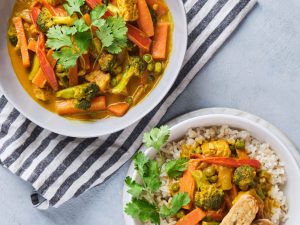 Vegetable yellow curry with tempeh strips served in bowls with brown rice