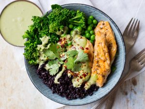 Chicken black rice bowl, one blue serving bowl filled with rice, marinated chicken, broccolini, peas and creamy herb sauce